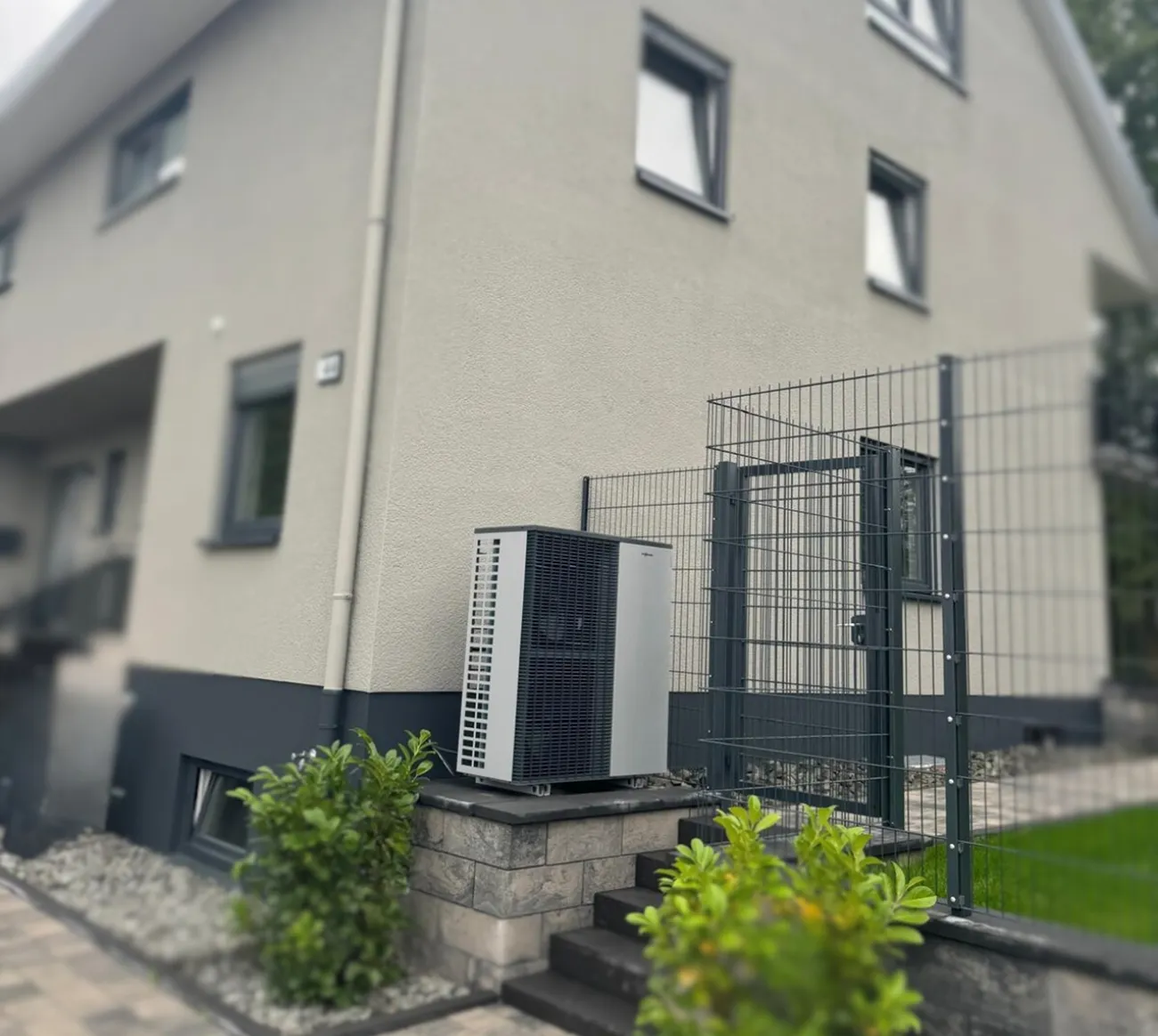 Außengerät einer Wärmepumpe vor einem Einfamilienhaus mit Gartentor