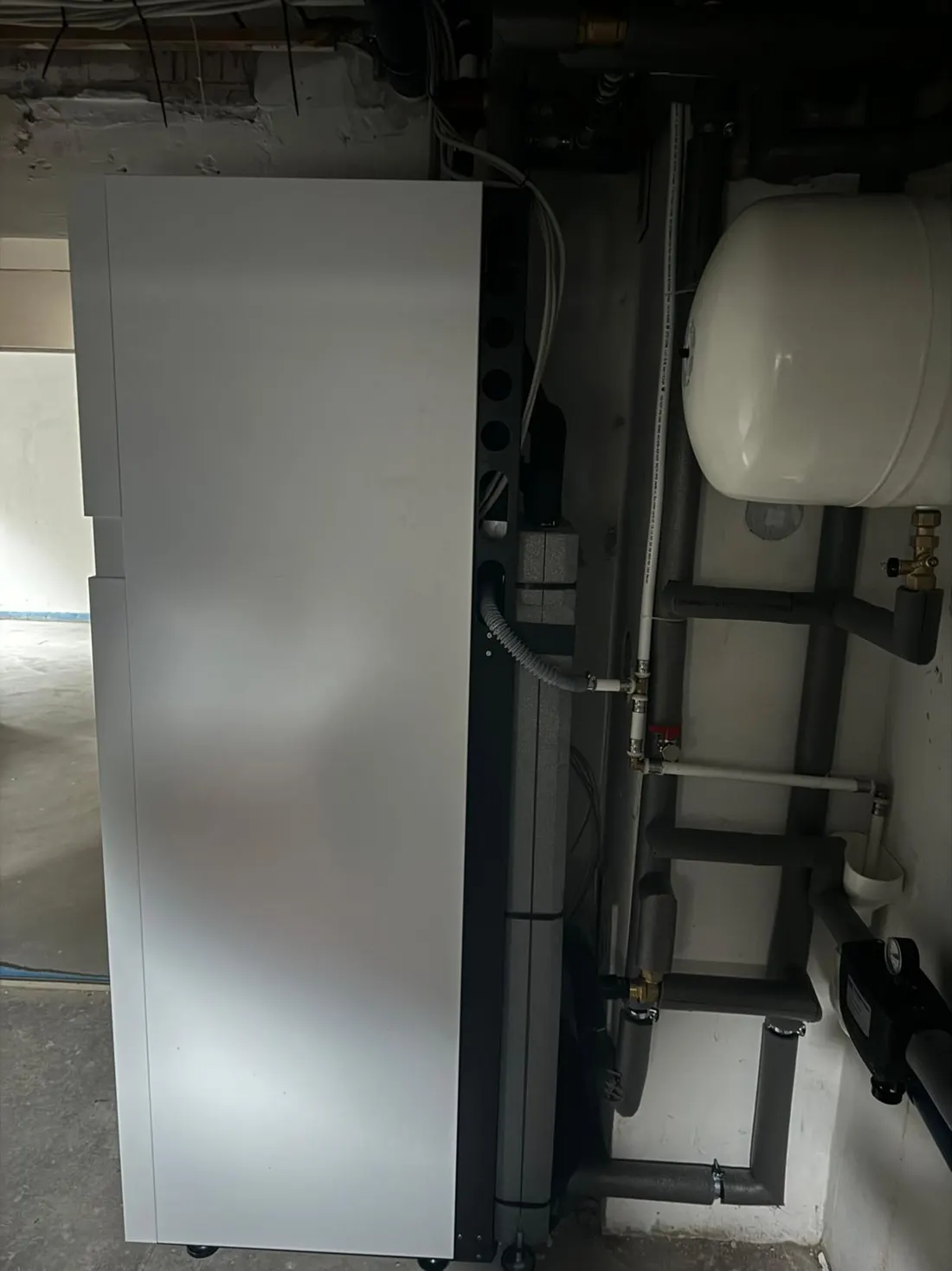 Weißer Wärmepumpen-Speicher im Heizraum neben Rohren und Ausdehnungsgefäß